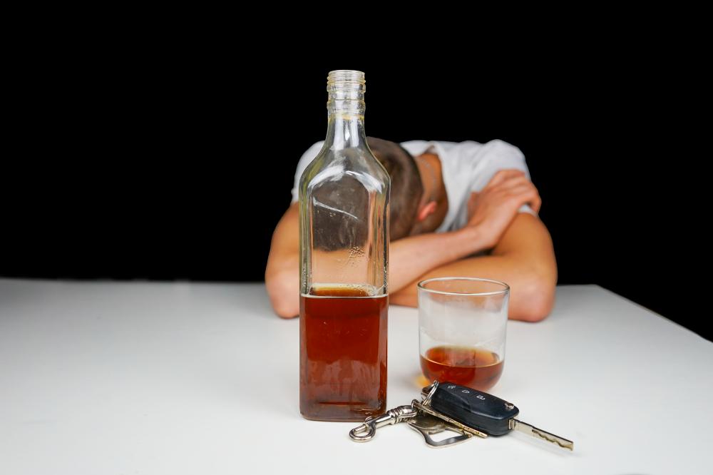 Drunk man asleep with car keys and alcohol, representing the need for detox and sobriety