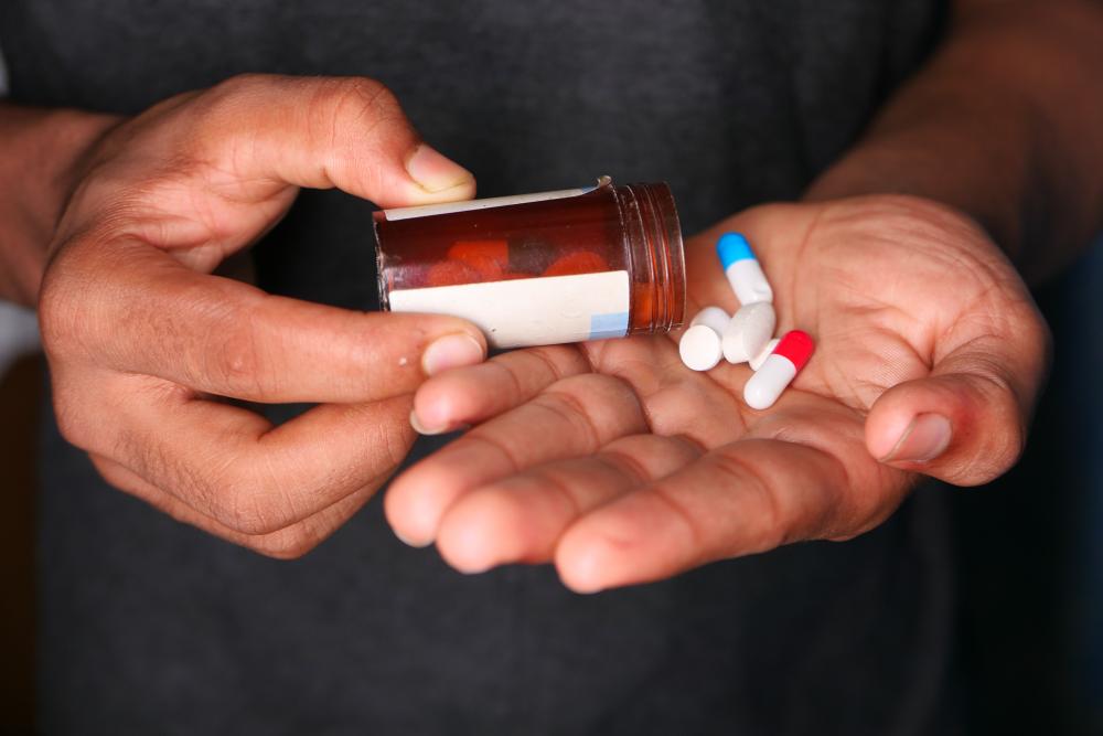 Hands holding pills on a black background symbolizing drug abuse treatment