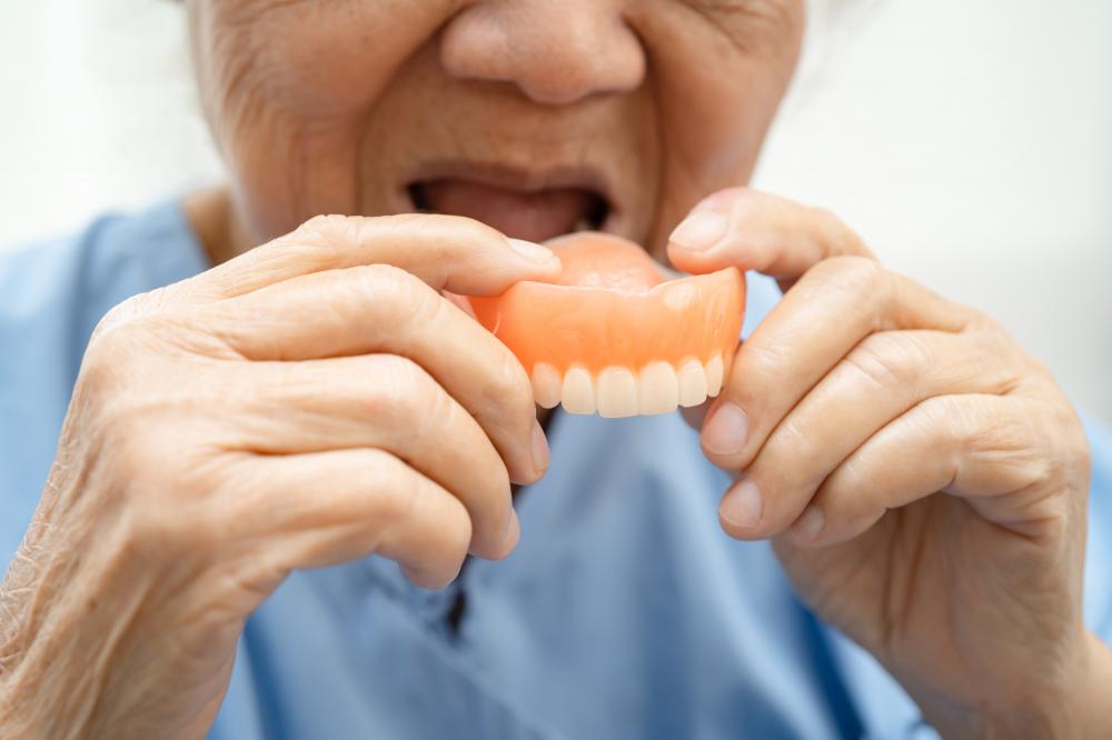 Asian elderly woman smiling with dentures in hand, symbolizing dental restoration