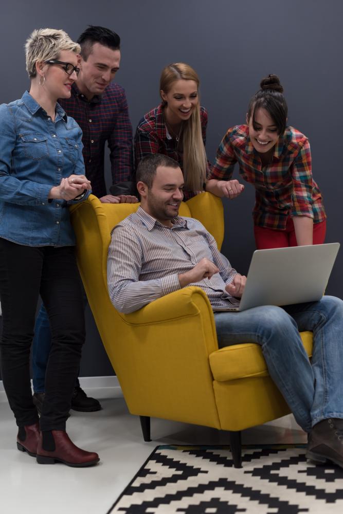 Group of five professionals engaging with a laptop in a modern office setting, highlighting collaboration and digital marketing strategies.