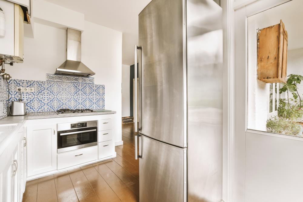 Stainless steel Thermador fridge freezer in modern kitchen with blue tile backsplash and wooden accents.
