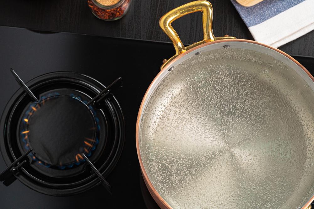 Copper pot with boiling water on a gas stove, surrounded by kitchen utensils and spices.