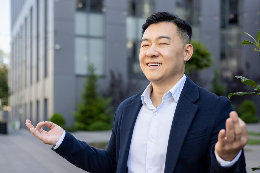 Young Asian male businessman smiling and gesturing outdoors, symbolizing confidence and positivity, relevant to Seattle SEO expert services.
