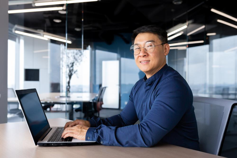 Young male Asian student studying at a laptop in a modern office setting, symbolizing the importance of digital marketing and SEO strategies in Seattle.