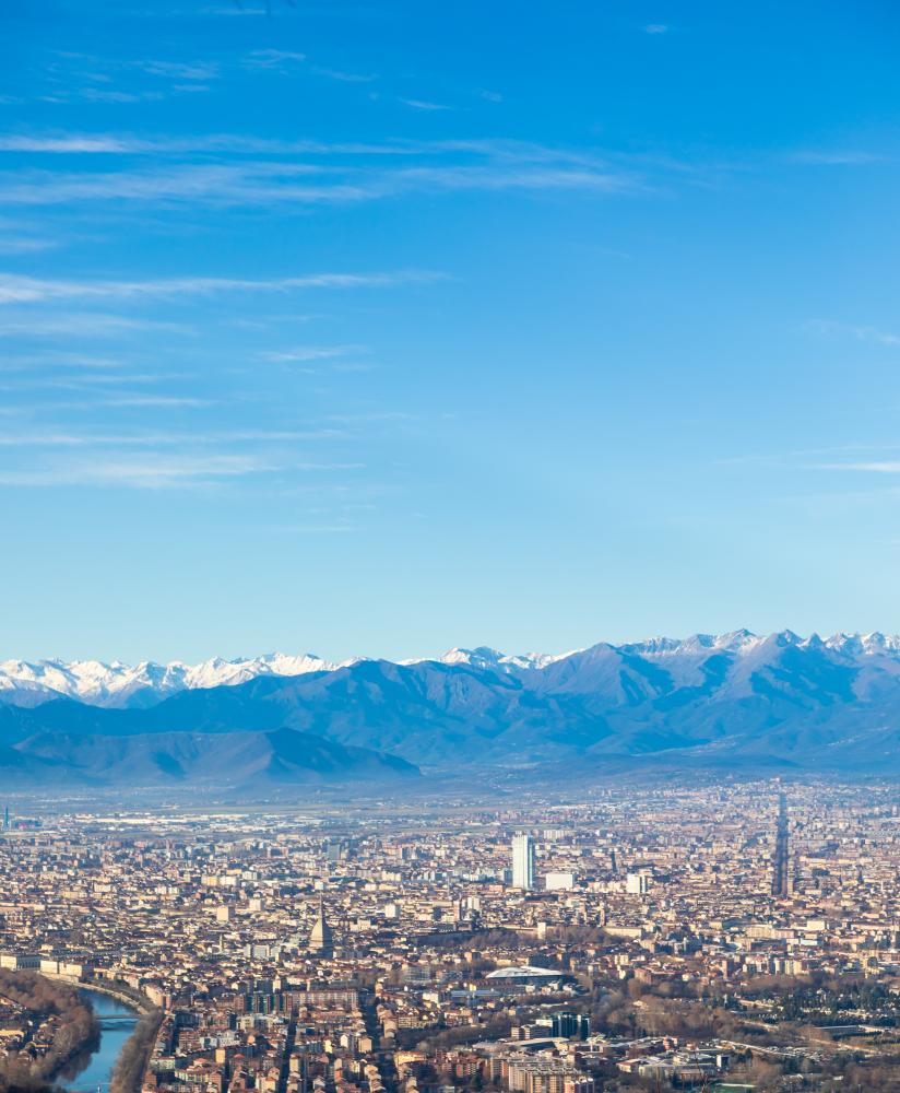 Panoramic view of Turin, Italy, featuring the city skyline with modern buildings and the Alps in the background under a clear blue sky, illustrating the importance of local visibility for SEO marketing strategies.